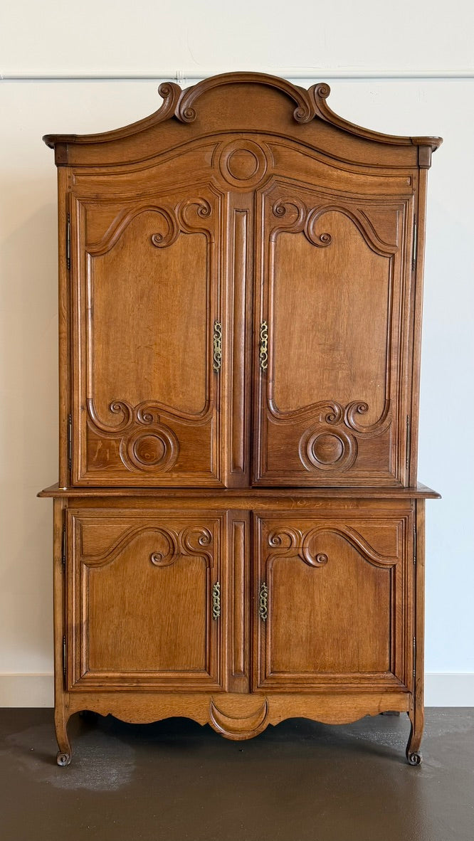An ornate vintage wooden cabinet with carved details, four doors, and curved legs, shown against a plain white wall and dark floor.
