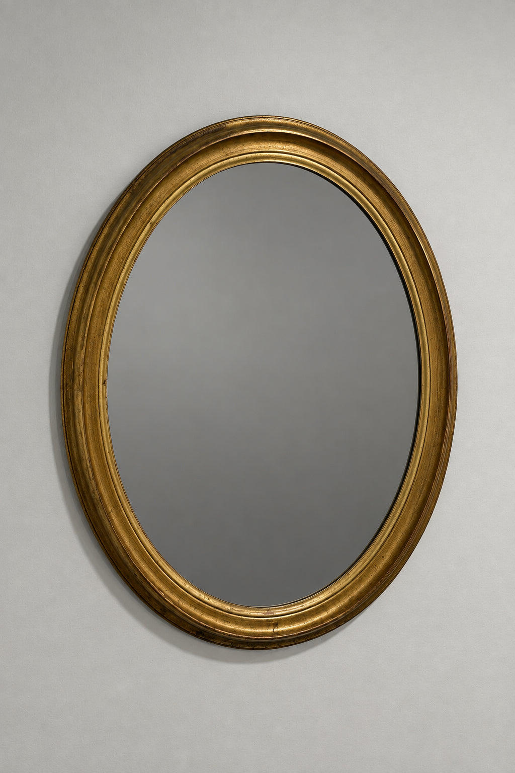 An oval wall mirror with a thick, ornate gold frame, mounted on a plain off-white wall.