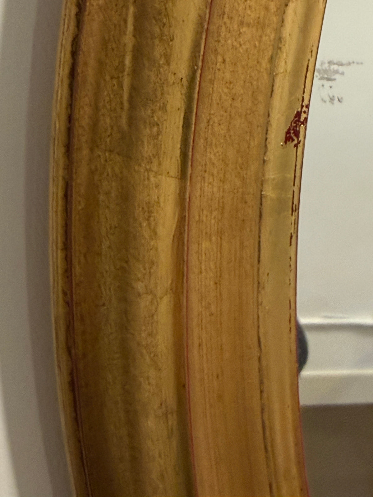 A close-up of a distressed gold picture frame showing the textured, worn wood grain and chipped edges against a white wall background.