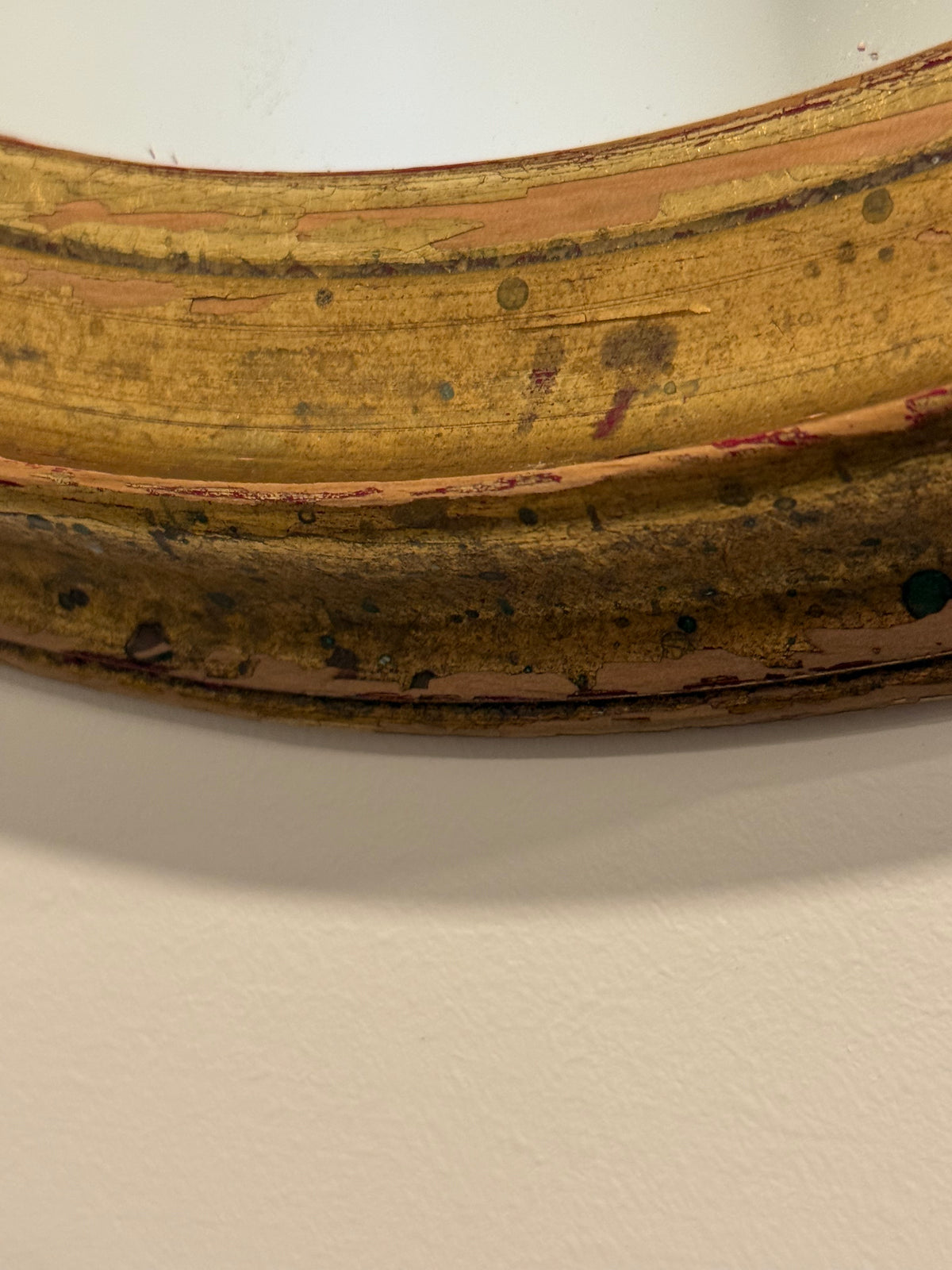A close-up detail shot of a distressed, vintage-style wooden frame with peeling yellow and brown paint, mounted on a plain off-white wall.