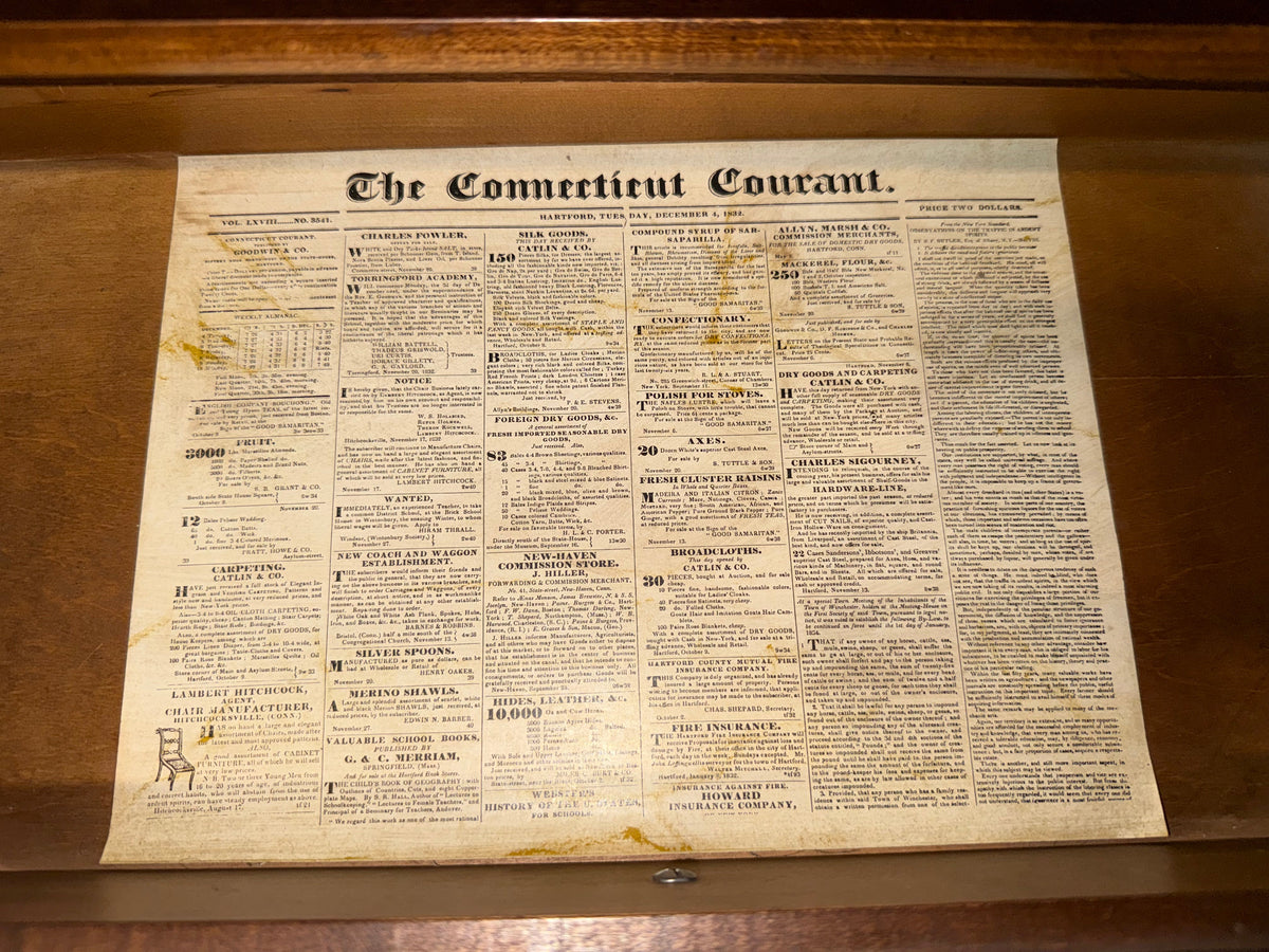An antique newspaper titled 'The Commercial Gazette' with aged, yellowed paper and dense columns of text, displayed flat against a dark wooden background.